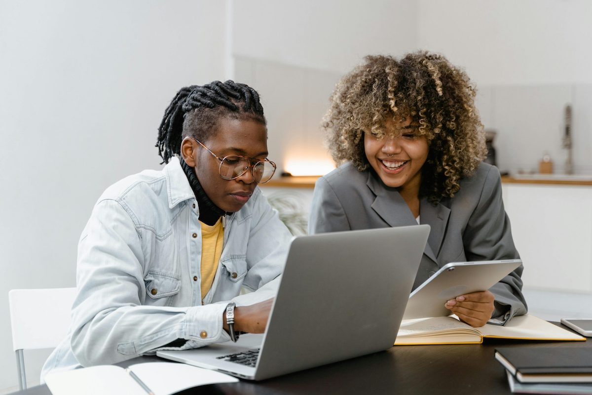 Two people sitting at a desk looking at a laptop computer.